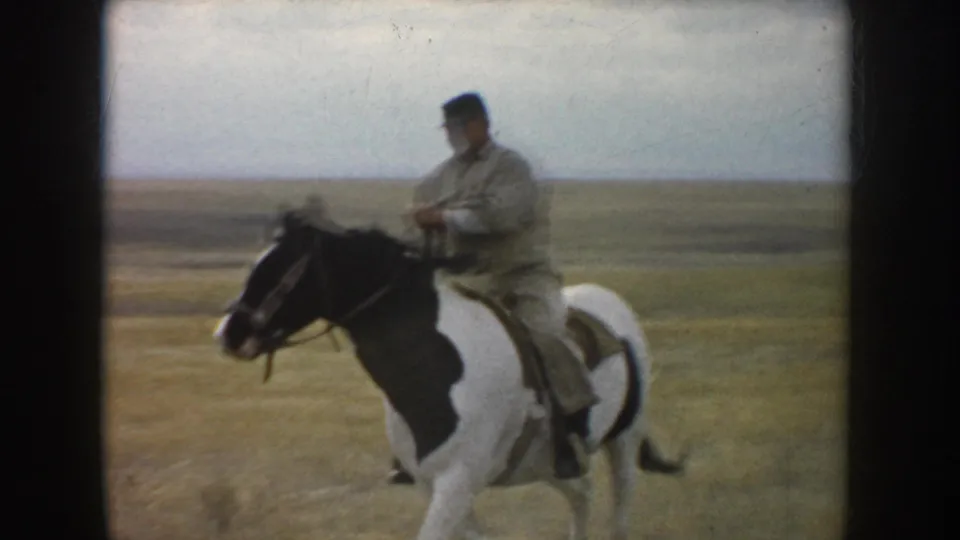 The adult rider turns the pinto horse sideways in the open South Dakota field, with flat prairie and pale sky behind them.