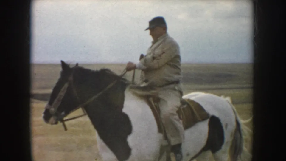 A closer 1953 South Dakota frame shows the rider in a cap holding the reins while seated on the pinto horse in the field.