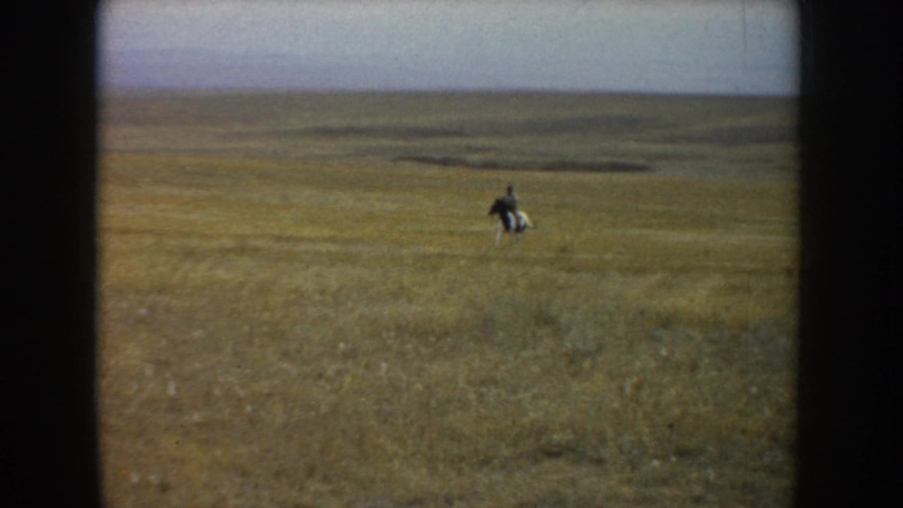 The rider and pinto horse appear small in the distance as they move across the broad South Dakota grassland.