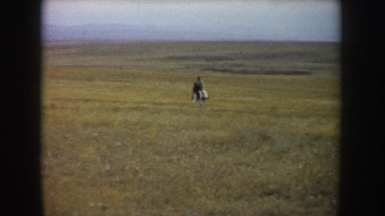 A man on a pinto horse appears small within the South Dakota prairie landscape, framed by dark 8mm film borders.