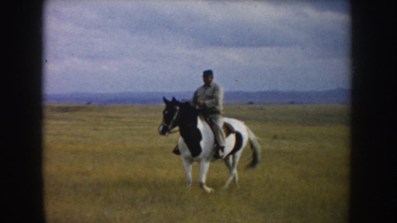 A man in light clothing rides a black-and-white pinto horse through a South Dakota prairie field in 1953 home-movie footage.