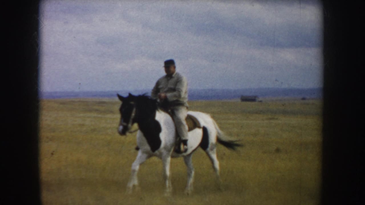 The rider and pinto horse appear nearer in the 1953 South Dakota prairie scene, with open grass and a cloudy sky behind them.