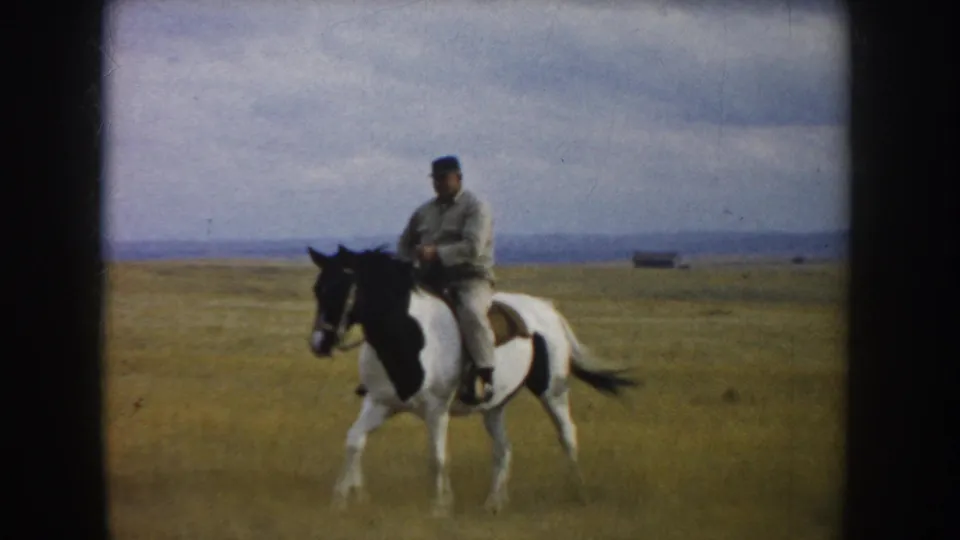 The rider and pinto horse appear nearer in the 1953 South Dakota prairie scene, with open grass and a cloudy sky behind them.