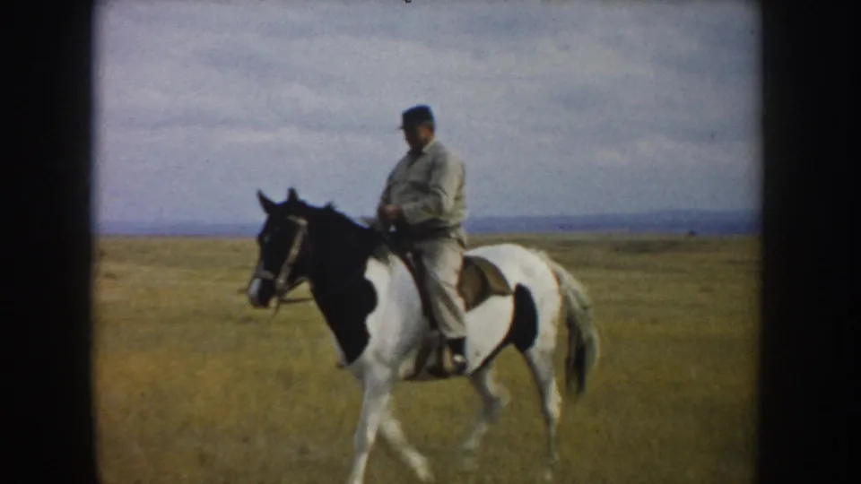 A closer 1953 South Dakota frame shows the rider seated on a pinto horse, with prairie grass, distant hills, and cloudy sky visible.