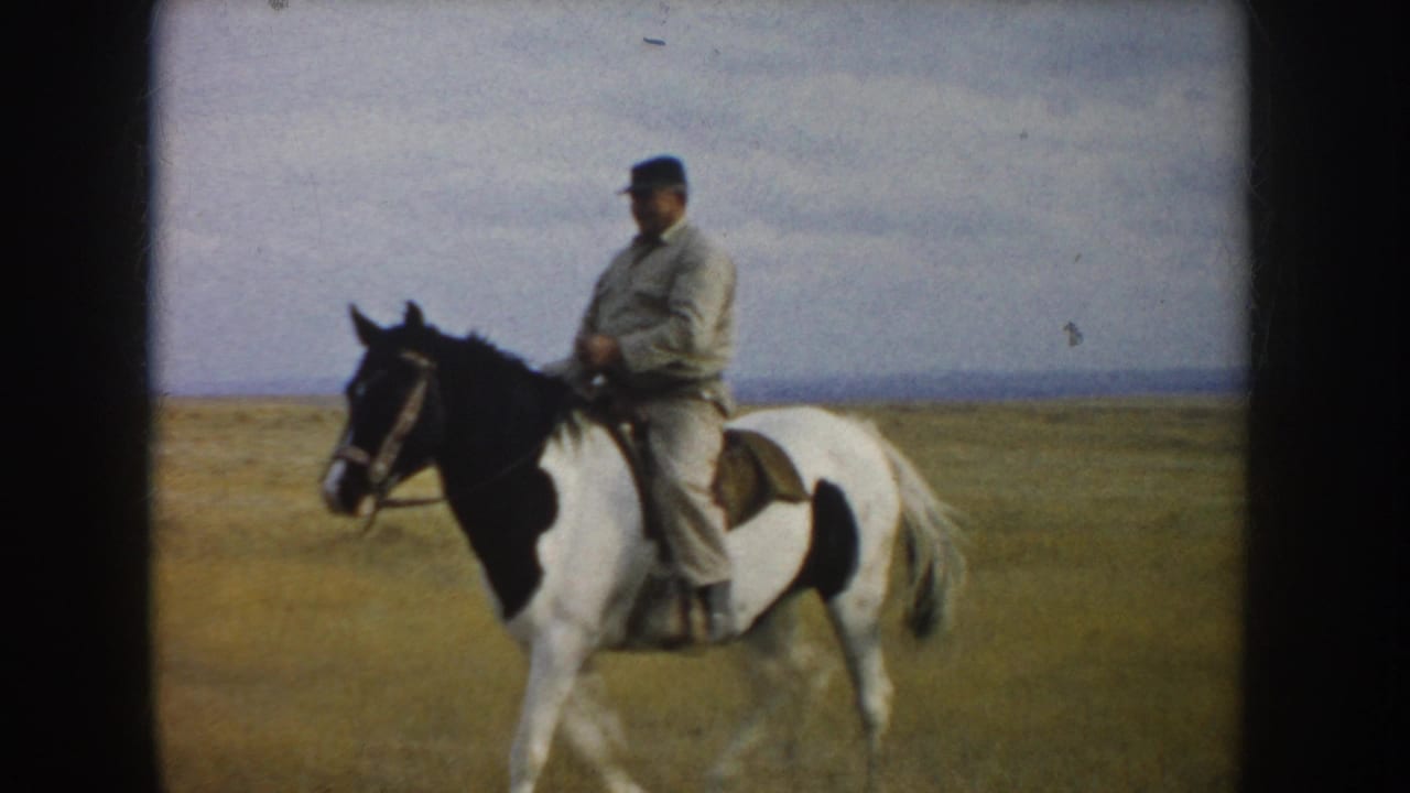 1953 South Dakota 8mm frame of a man in light clothing riding a pinto horse across an open grassy plain.