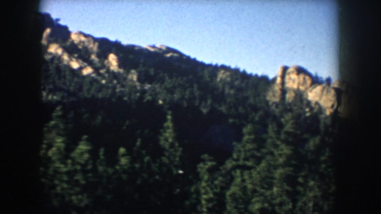 Forested mountain ridge with rocky outcrops beneath a clear blue sky.