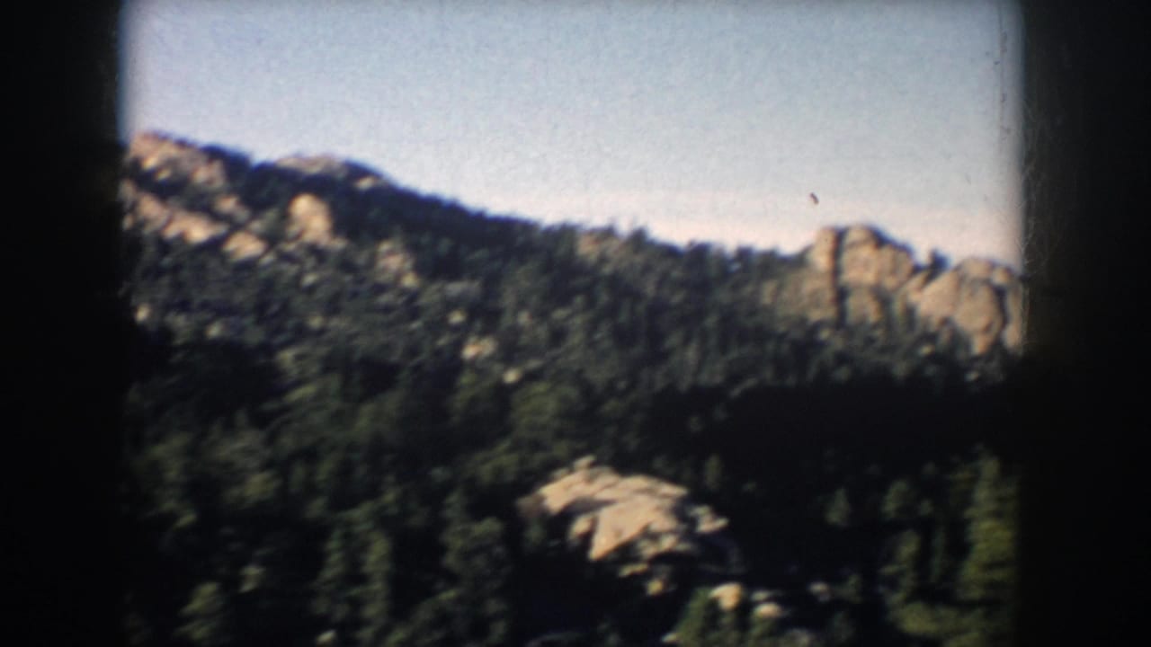South Dakota 8mm frame from 1953 showing forested uplands, scattered rocky plateaus, and a clear sky from a moving viewpoint.