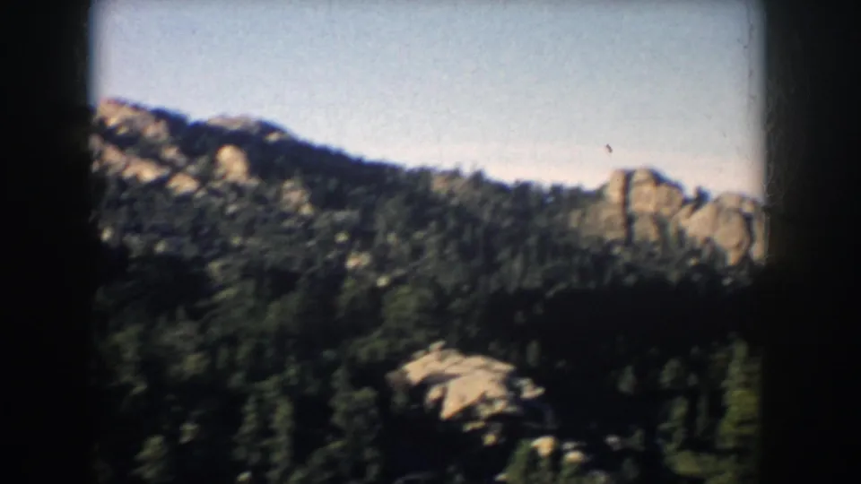 South Dakota 8mm frame from 1953 showing forested uplands, scattered rocky plateaus, and a clear sky from a moving viewpoint.