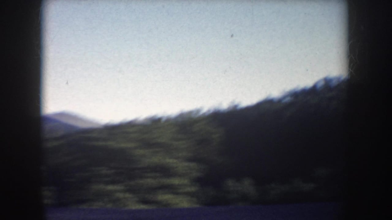 Wooded hills and distant ridge seen through dark vehicle framing.