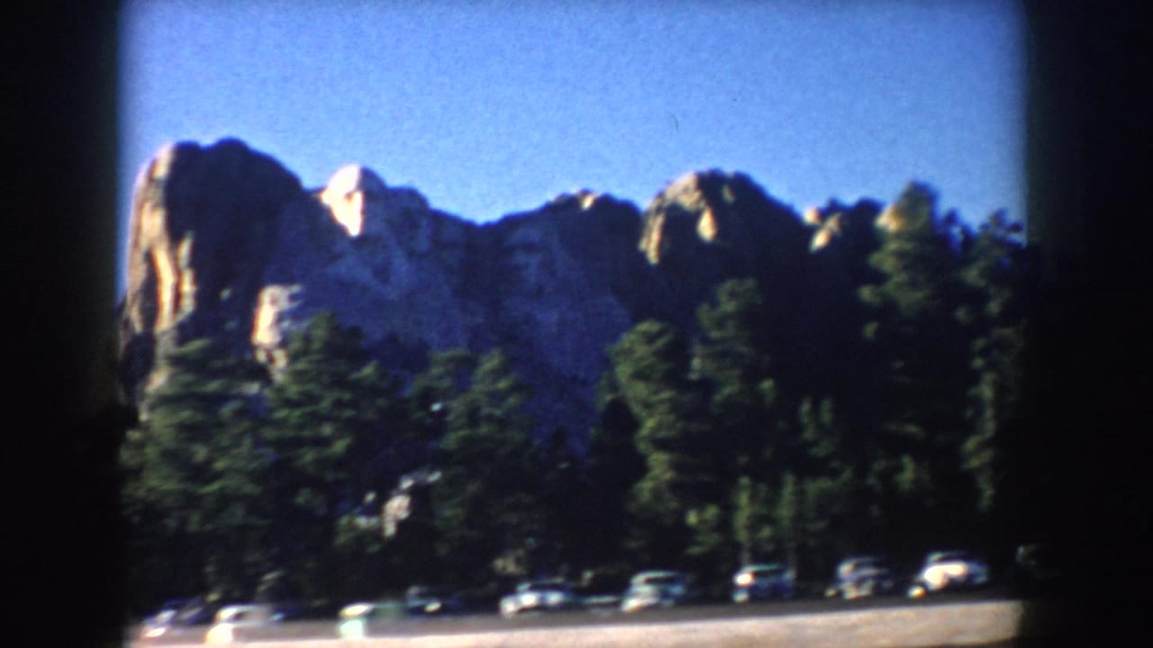 Mount Rushmore and forest with several cars along the lower edge of the frame.