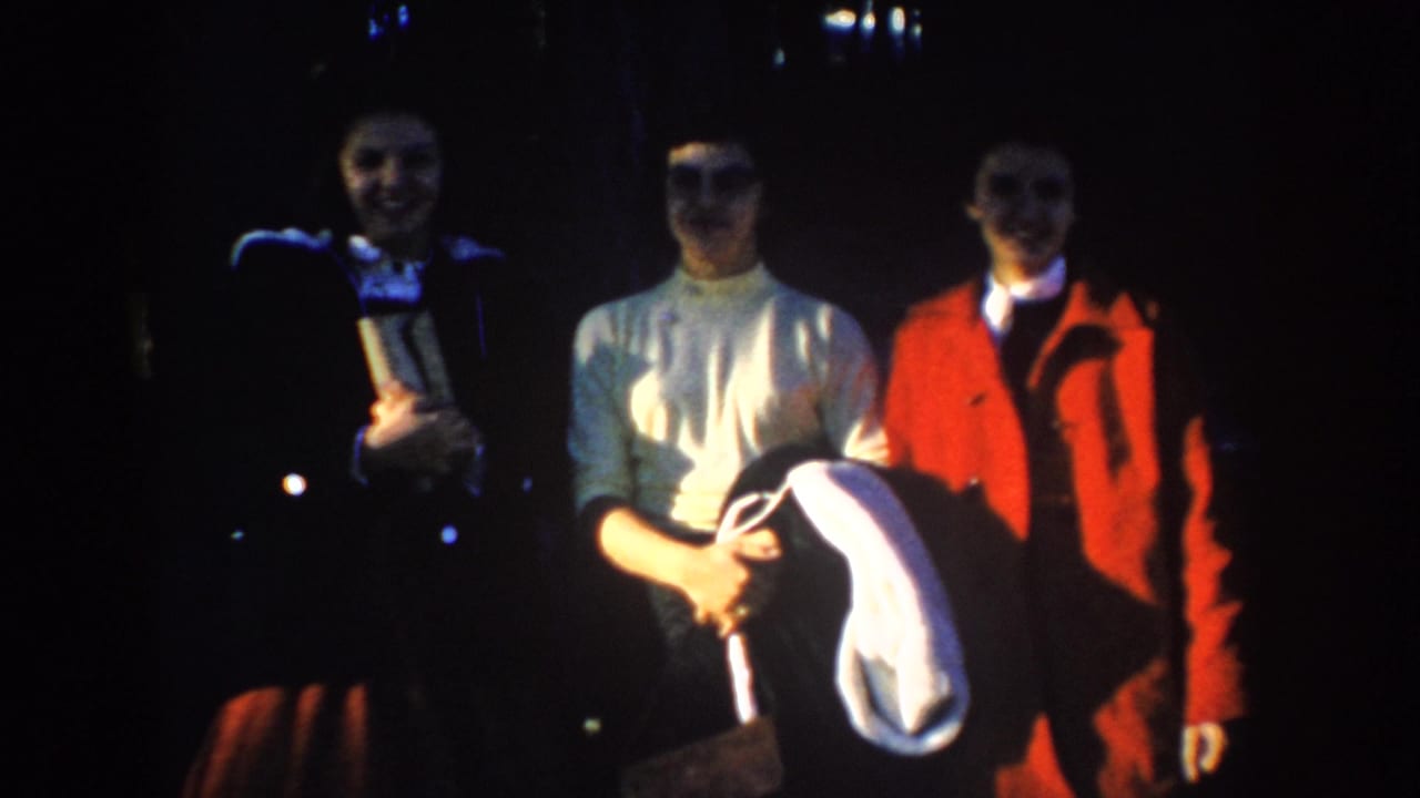 Three women in period clothing stand outdoors in a dark home-movie frame, likely part of the 1953 South Dakota vacation footage.