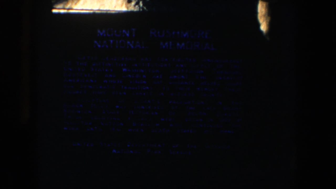 A low-light 8mm frame shows the Mount Rushmore National Memorial plaque in South Dakota.