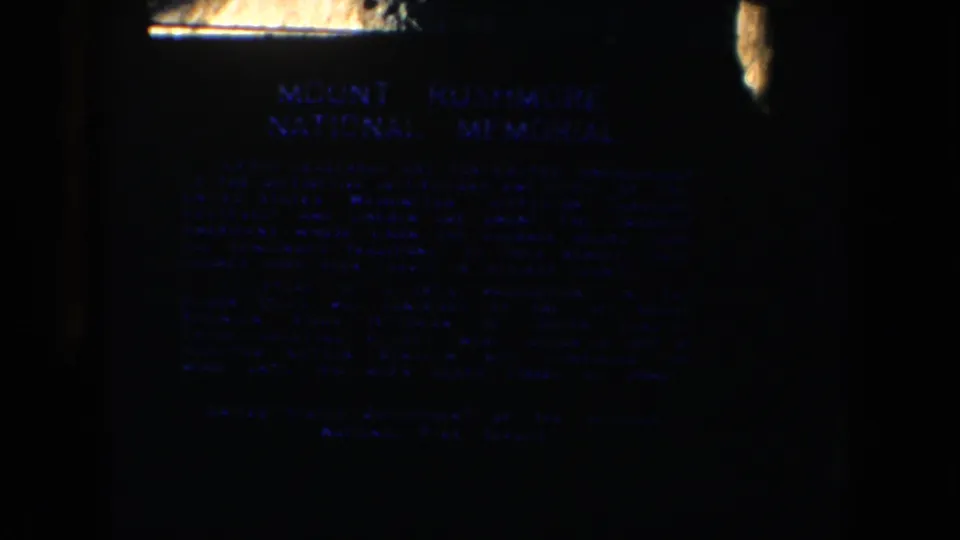 A low-light 8mm frame shows the Mount Rushmore National Memorial plaque in South Dakota.