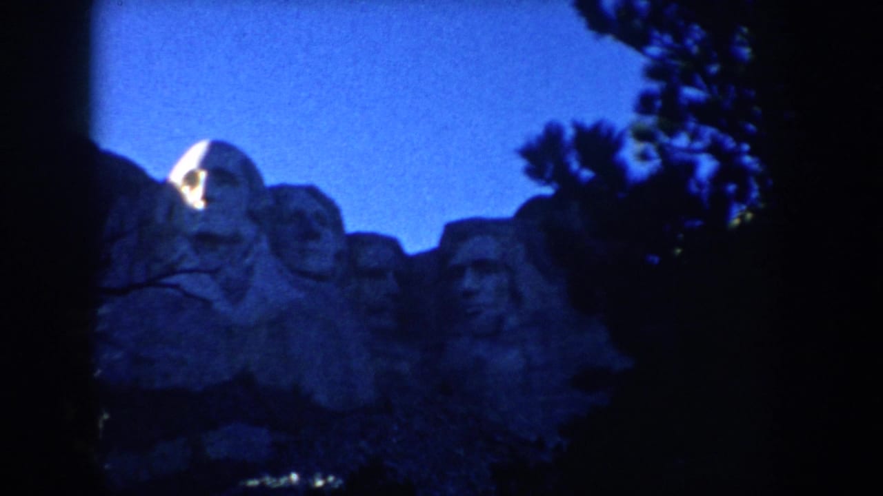 1953 South Dakota home-movie view of Mount Rushmore at night, with illuminated carved faces and silhouetted trees.