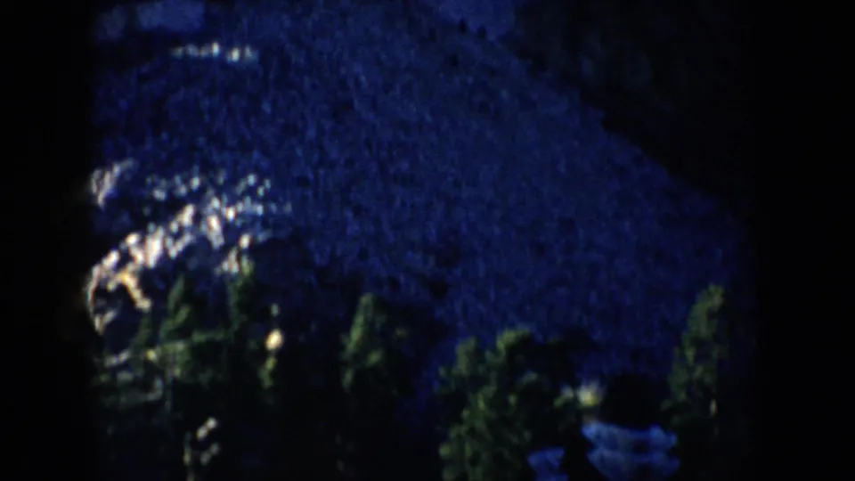 1953 South Dakota 8mm frame of a snowy wooded area at night with a small bundled figure near the lower right.