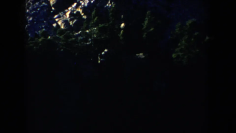 1953 South Dakota 8mm frame showing dark snowy woods at night with a small bundled figure partly visible on the right.
