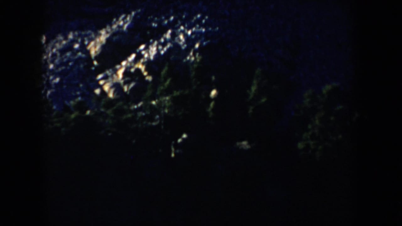 1953 South Dakota 8mm frame showing Mount Rushmore in heavy shadow, with only portions of the carved heads catching light.