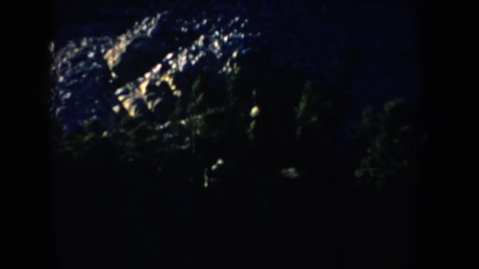 1953 South Dakota 8mm frame showing Mount Rushmore in heavy shadow, with only portions of the carved heads catching light.