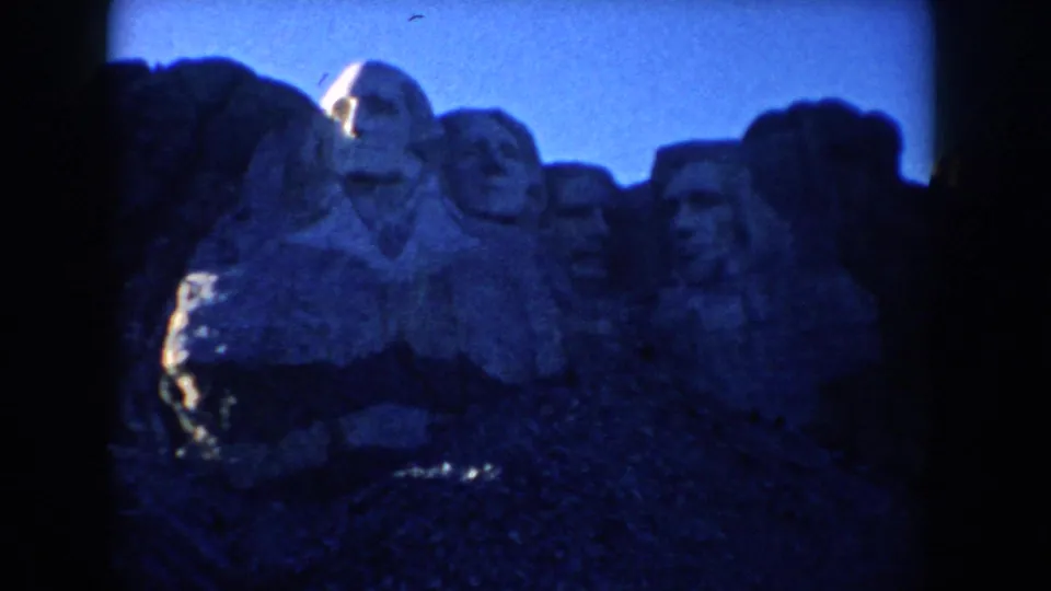 1953 South Dakota 8mm frame showing Mount Rushmore from a low visitor angle beneath a bright blue sky.