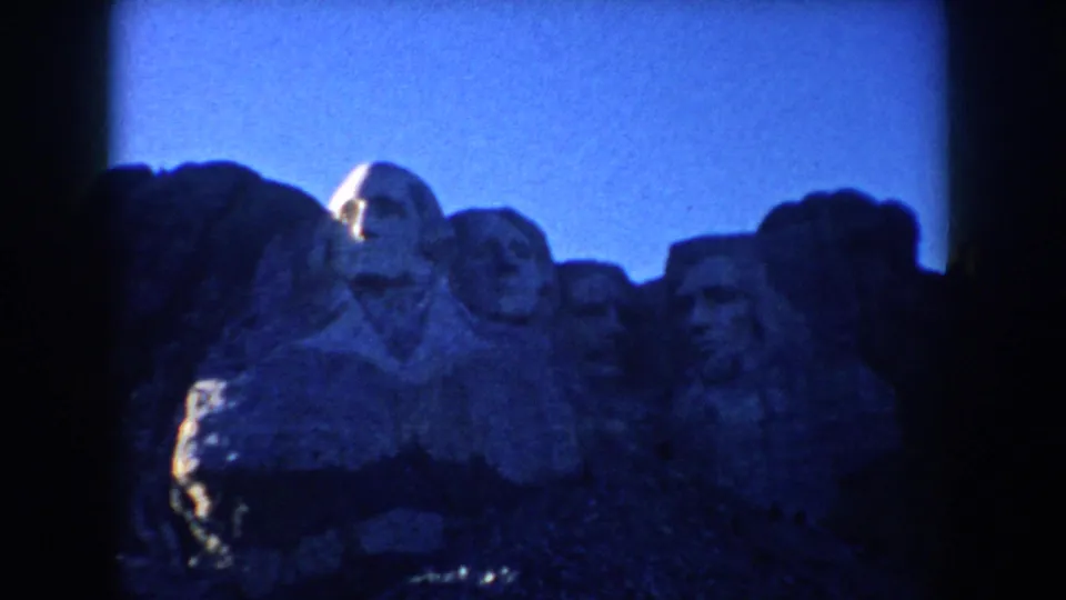 1953 South Dakota 8mm frame of Mount Rushmore, showing the carved presidential heads in high-contrast light and shadow.