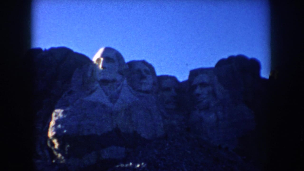 1953 South Dakota home-movie frame showing the Mount Rushmore presidential carvings under a deep blue sky.