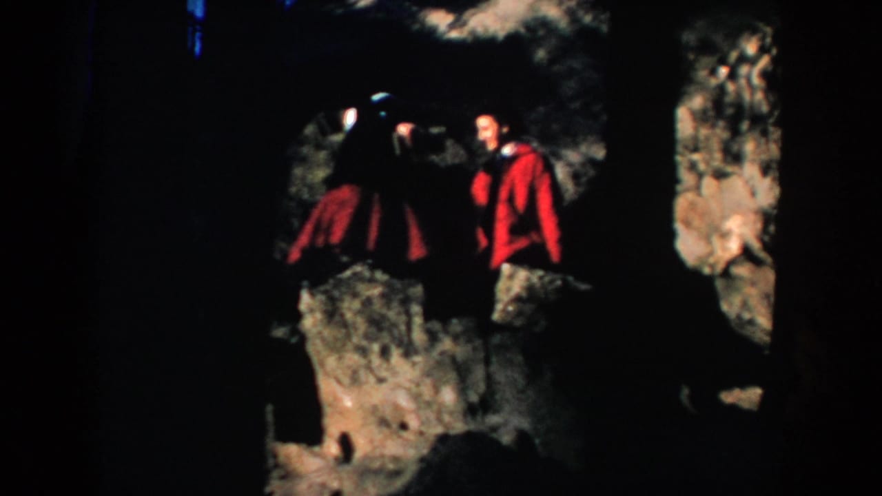 Two adults move or pose near rocks with heavy shadow around them.