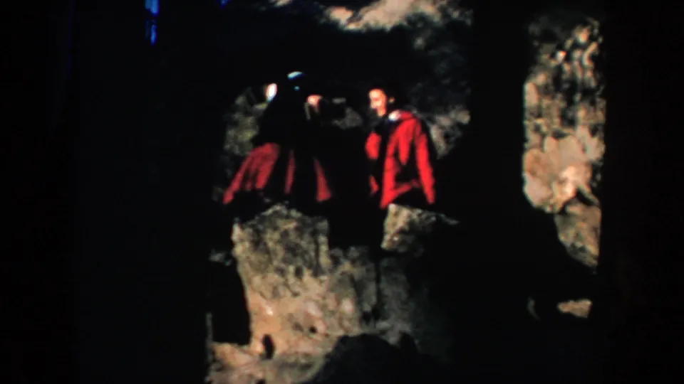 Two adults, one in a red coat and one in dark clothing, stand on rocky South Dakota terrain in a 1953 home movie.