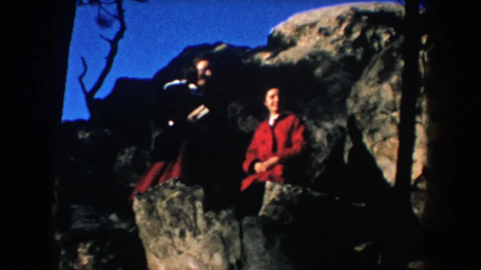 Two adults stand on a rocky outcrop against blue sky in South Dakota footage dated 1953.