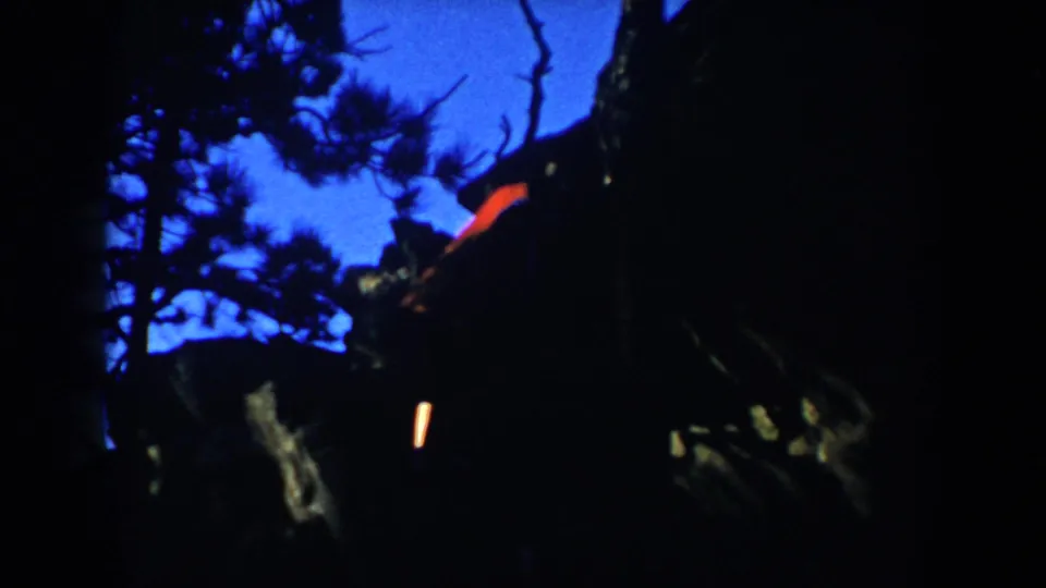 Underexposed South Dakota 8mm frame with silhouetted trees, blue sky, and an indistinct person or red garment near stairs.