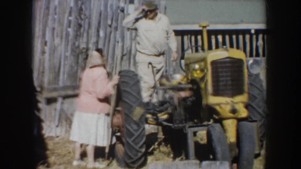 A woman in a pink top and a man in work clothes stand by a yellow tractor on a South Dakota farm in 1953 footage.