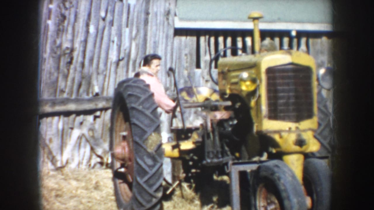 Man beside a yellow tractor in front of a weathered wooden barn.