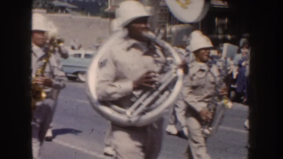 Close home-movie view of a helmeted sousaphone or tuba player marching with a uniformed band in South Dakota.