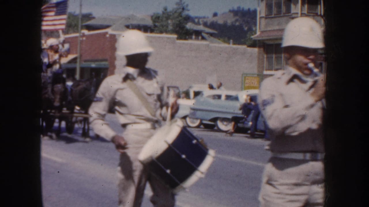 A drummer and horn player march past cars and storefronts during the parade.