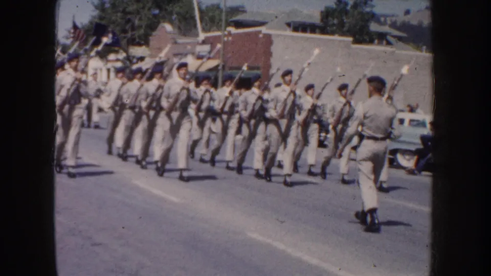 1954 South Dakota parade scene with cadets in light uniforms marching down a street with rifles and fixed bayonets.