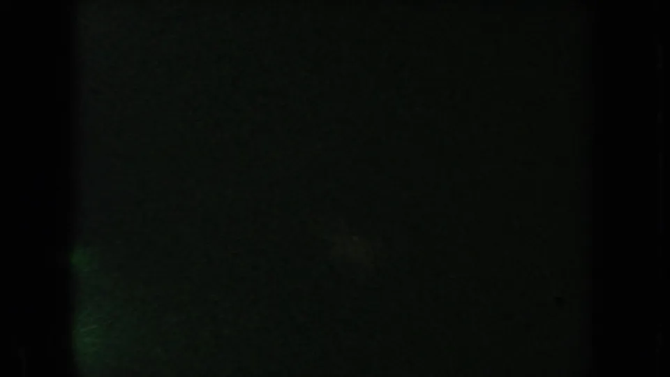 Very dark 8mm frame from the South Dakota reel, with faint green exposure, grain, and vertical film-edge shadowing.