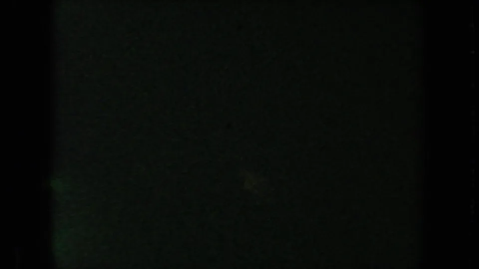 Underexposed 1954 8mm frame with green-black tone, grain, and a faint vertical film boundary but no clear subject.