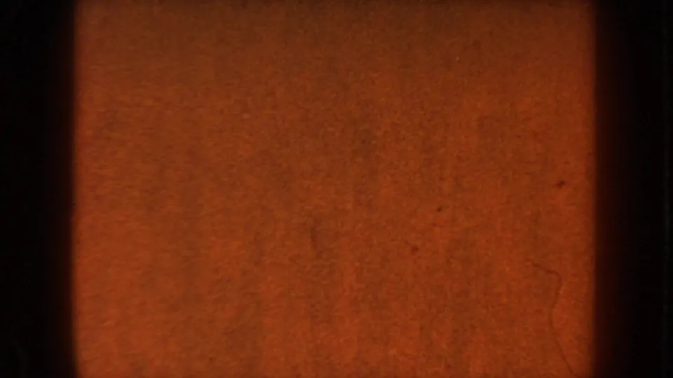 Orange-tinted end or leader-like 8mm frame from the 1954 reel, showing grain, dust specks, and dark film-edge shadows.