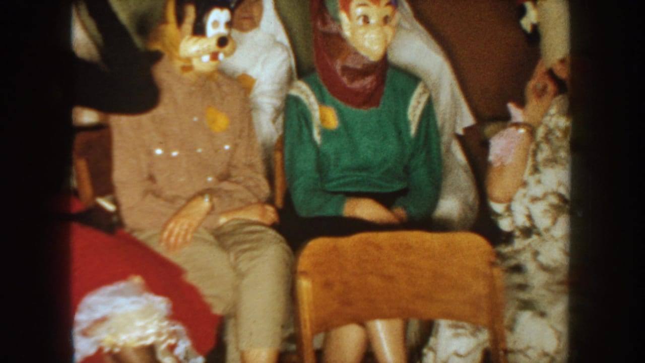 1954 South Dakota party frame with adults wearing novelty masks and scarves while seated closely in a private room.