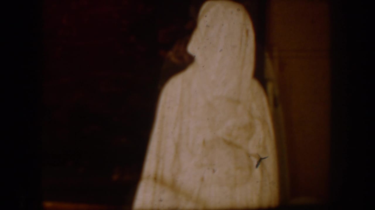A tall white-robed religious figure stands against a dark interior background.