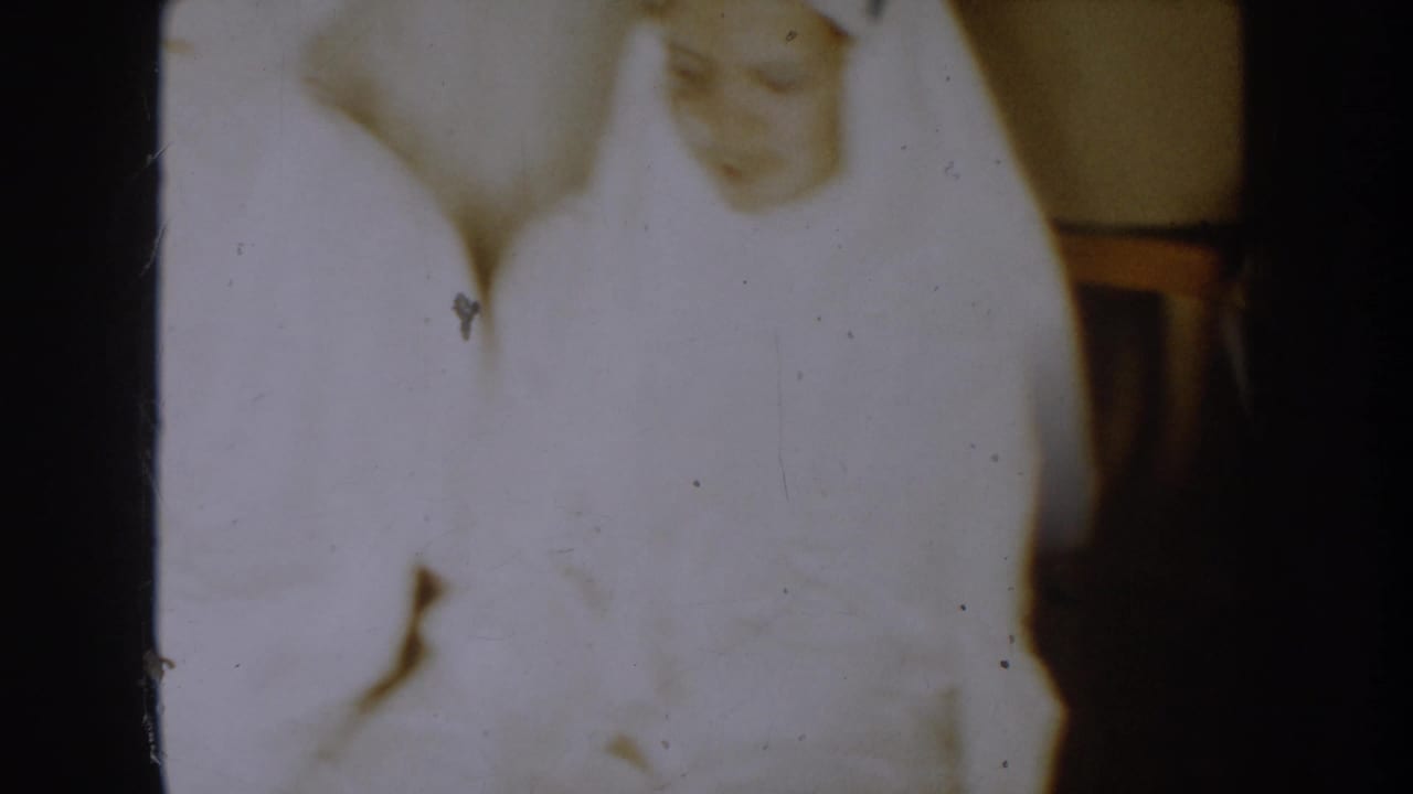 Soft 8mm frame from the 1954 South Dakota clip showing a person in a white robe costume inside a private room.