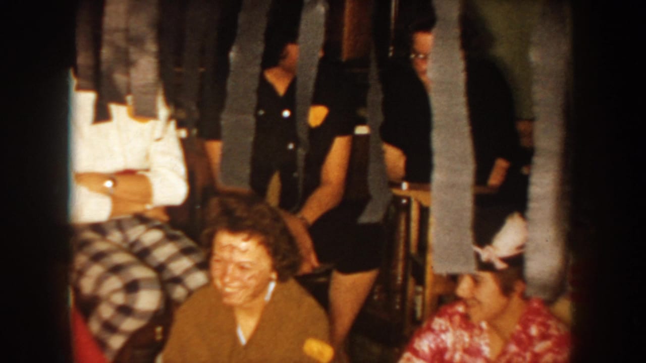 Smiling party guests sit near streamers, including a woman in a brown sweater.