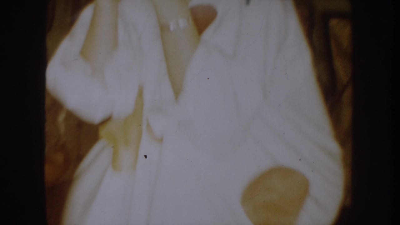 1954 South Dakota home-movie frame showing a person in a white costume partly covering their face inside a private room.