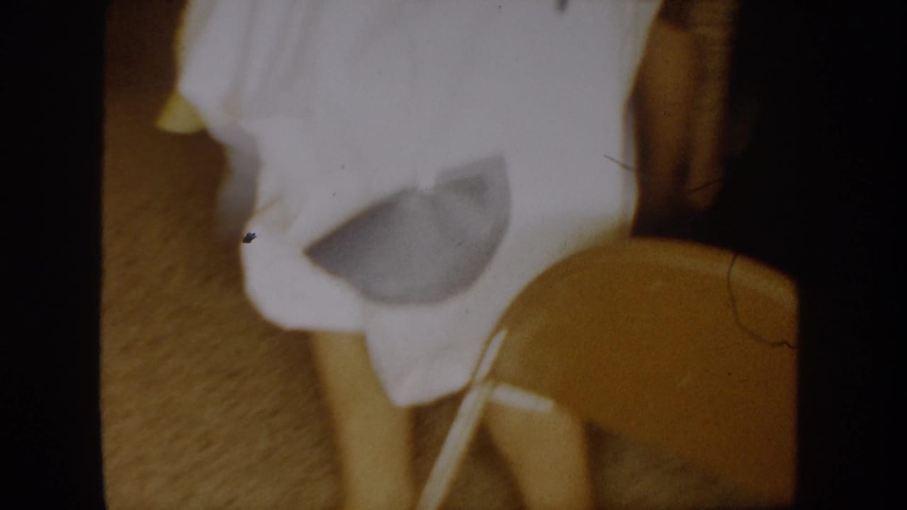 White-costumed person near a chair with face mostly hidden by motion and fabric.