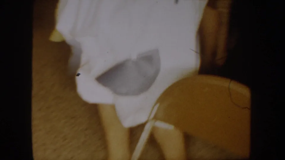 1954 South Dakota party footage frame with a white-costumed person moving near a chair in a private interior.