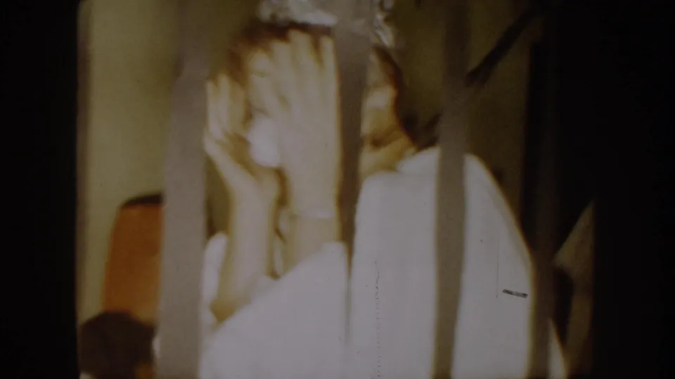 1954 South Dakota interior frame showing a person in white covering their face beside a vertical post or furniture edge.