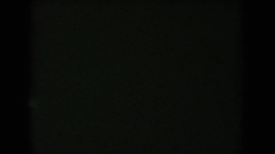 Mostly dark 8mm frame with faint greenish texture, likely between visible moments in the short home-movie clip.