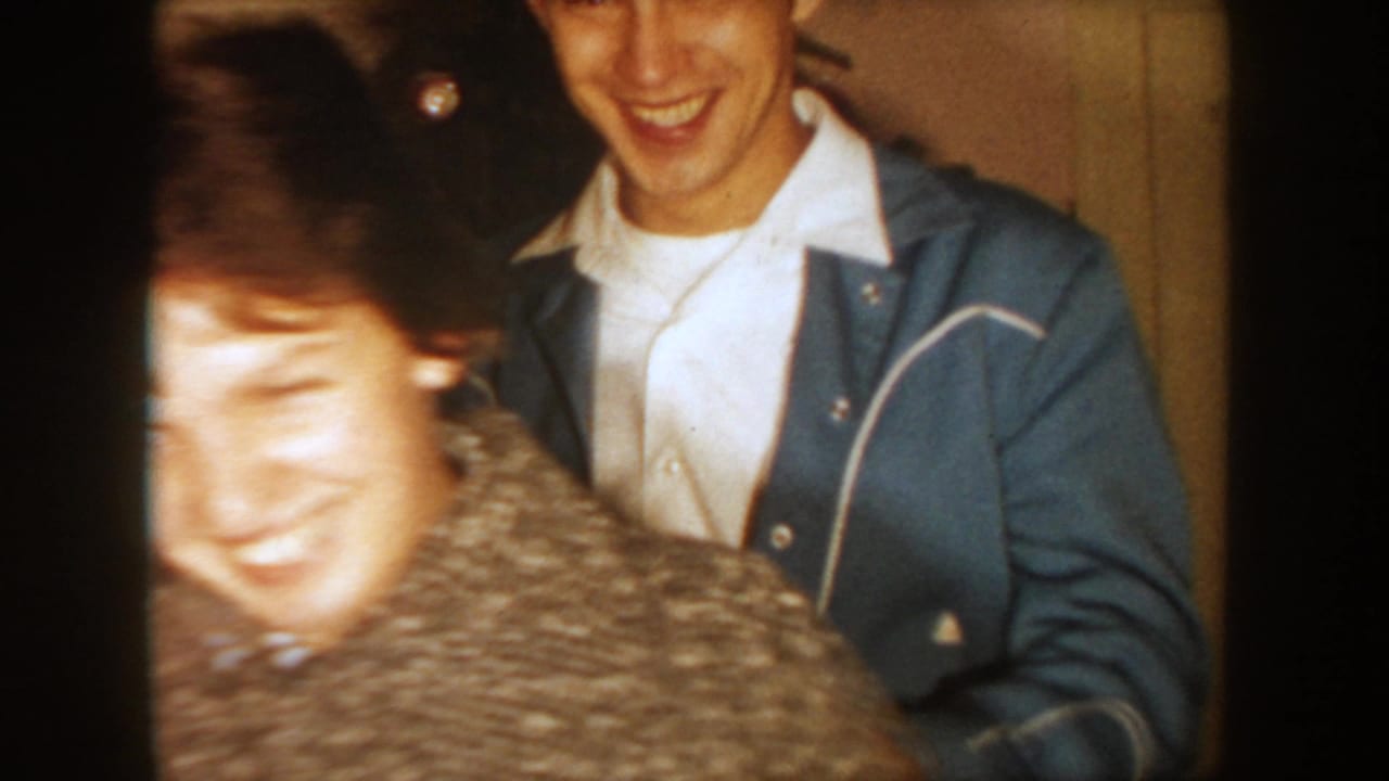 1954 South Dakota frame with a laughing man in a blue jacket and a motion-blurred woman near the Christmas tree.