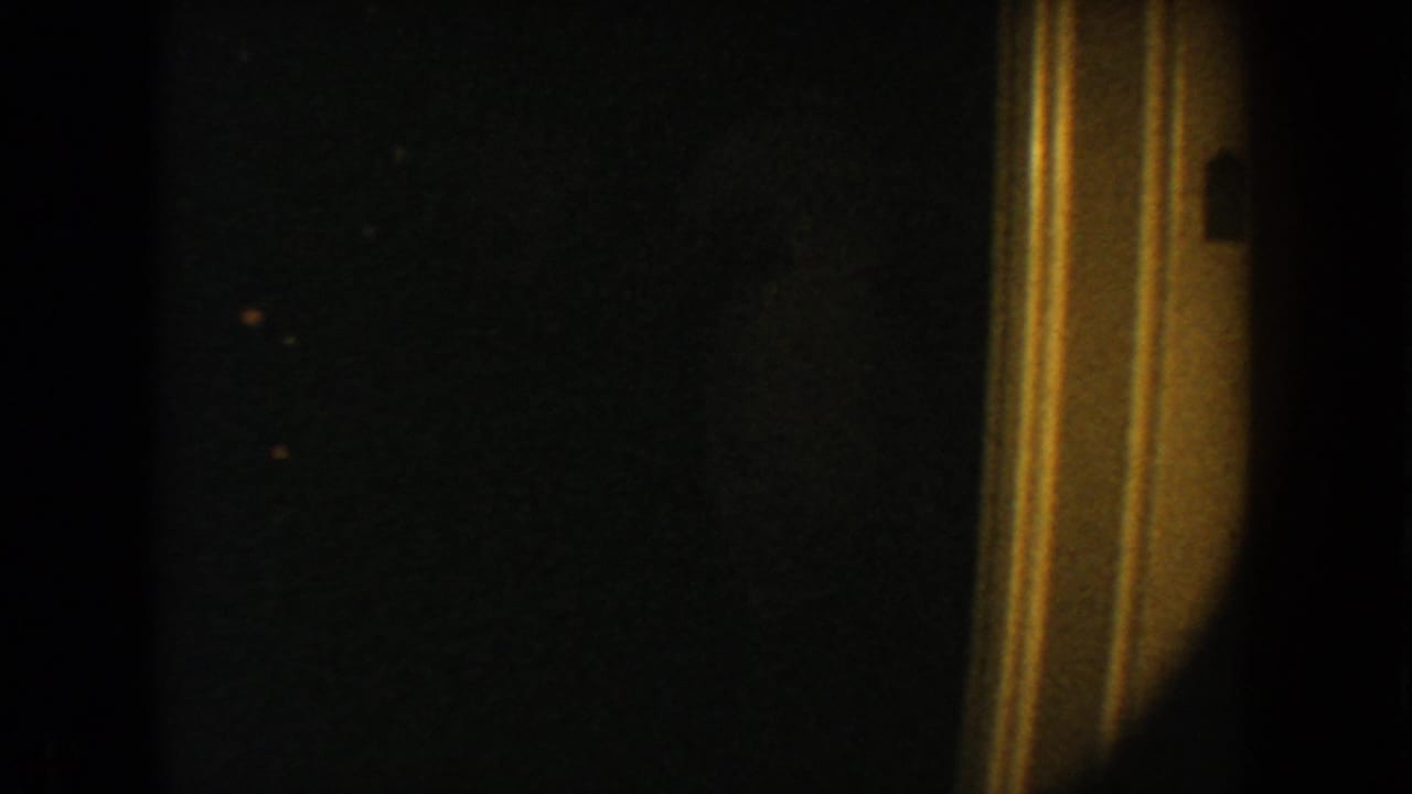 1954 South Dakota 8mm frame showing a very dark interior view beside warm-toned vertical door trim.