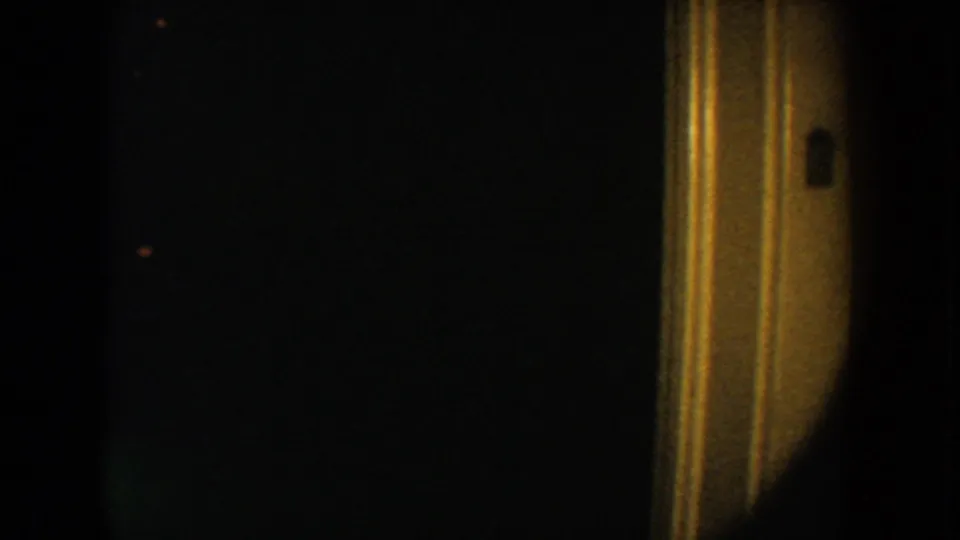 1954 South Dakota 8mm frame showing warm vertical trim, a small dark rectangular detail, and heavy low-light grain.