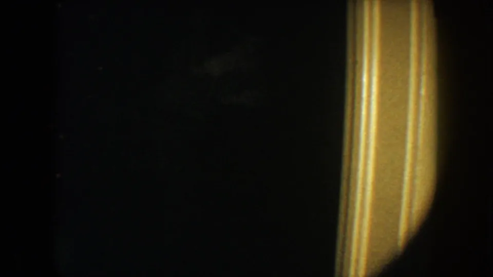 1954 South Dakota home-movie frame with a dark doorway, yellow trim, and a faint light-toned figure or garment in shadow.
